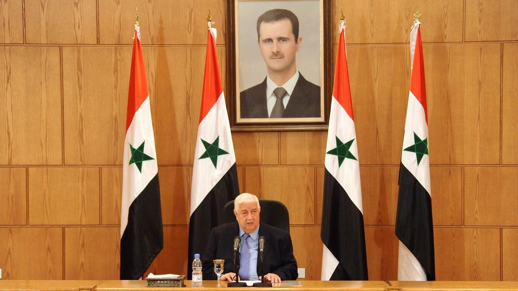Walid Muallem below a photo of Bashar al-Assad