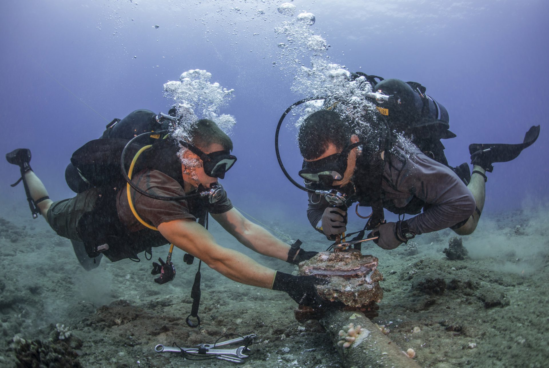 Chief Construction Electrician Daniel Luberto, right, and Construction Mechanic 3rd Class Andersen Gardner, assigned to Underwater Construction Team 2, Construction Dive Detachment Bravo (UCT2 CDDB), remove corroded zinc anodes from an undersea cable at the Pacific Missile Range Facility Barking Sands, Hawaii.