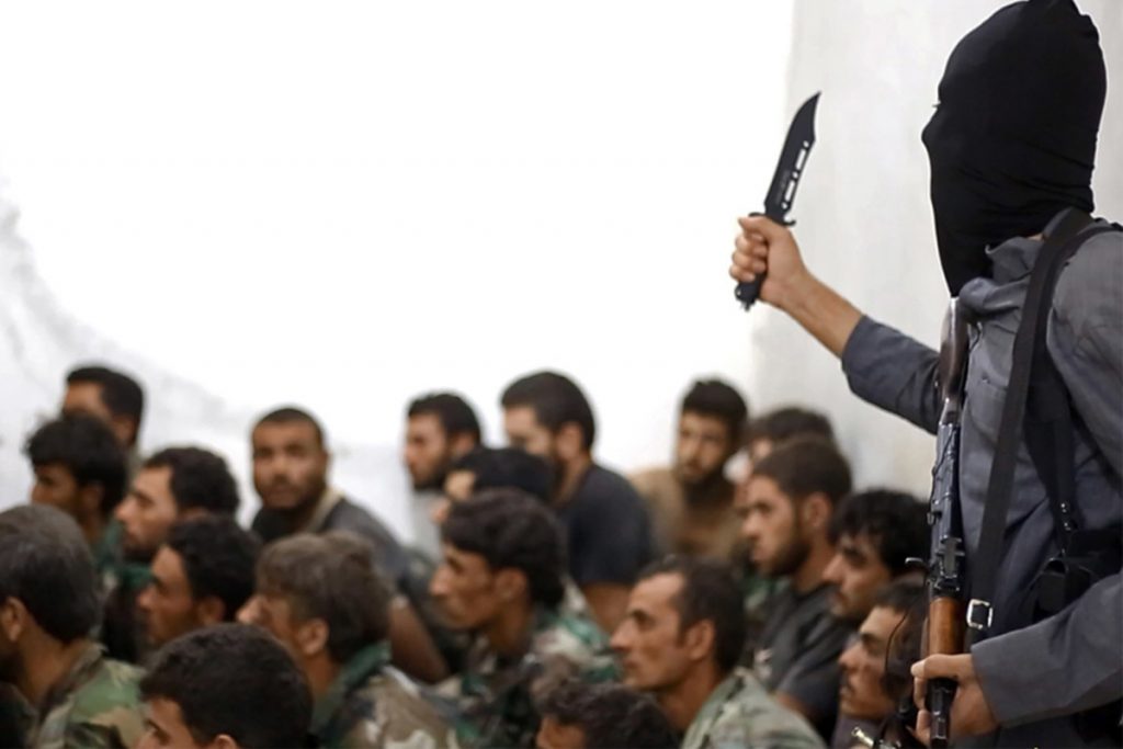 A fighter from ISIS, armed with a knife and an automatic weapon, next to captured Syrian army soldiers and officers, following the battle for the Tabqa air base in Raqqa, Syria.