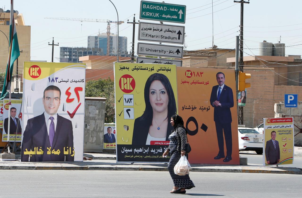 A Kurdish woman walks past campaign posters ahead of regional elections, in Erbil