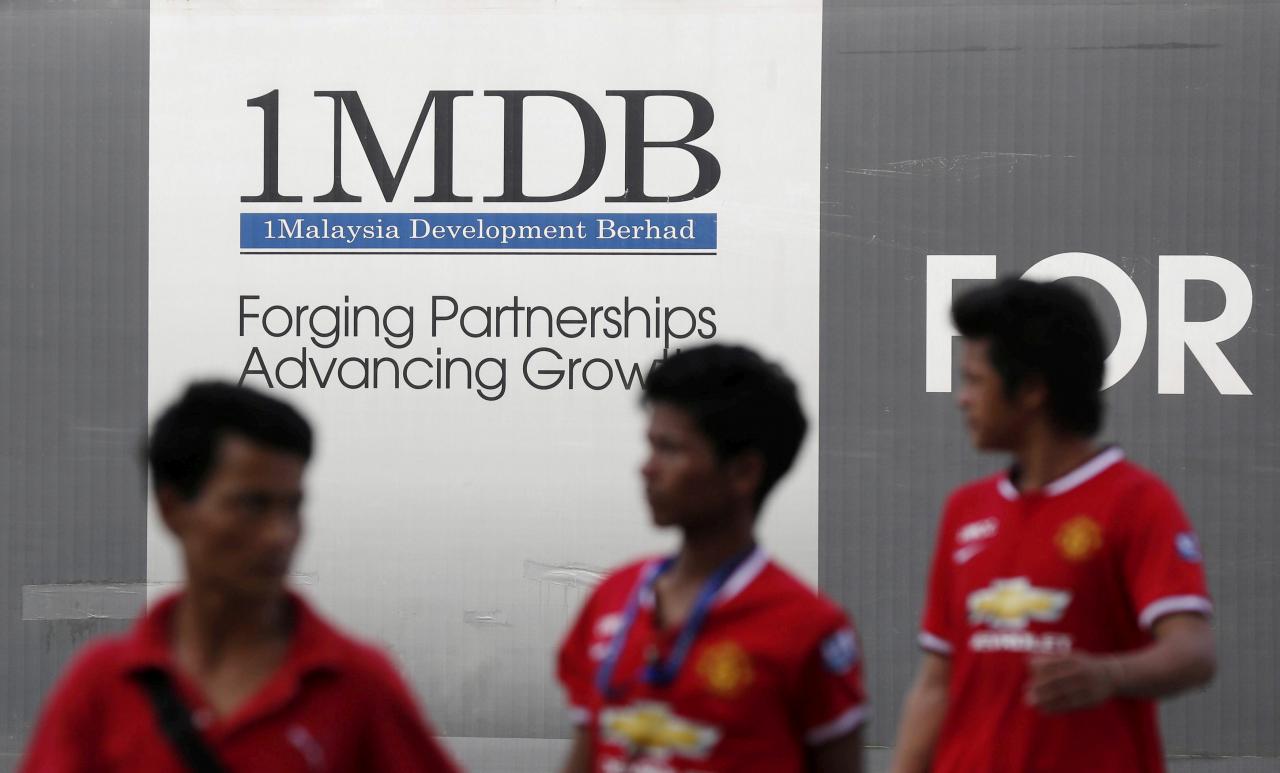 FILE PHOTO: Men walk past a 1 Malaysia Development Berhad (1MDB) billboard at the fund’s flagship Tun Razak Exchange development in Kuala Lumpur