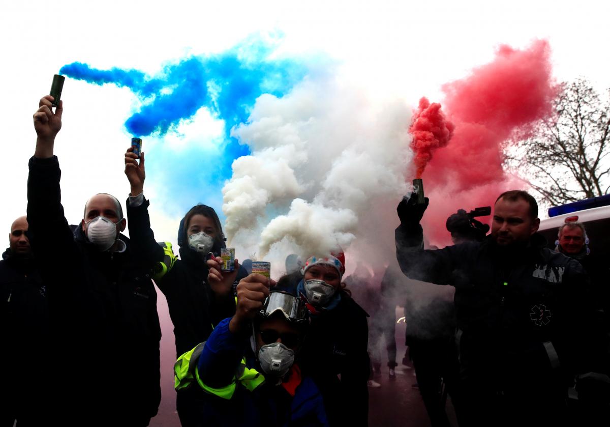 French ambulance drivers hold blue, white, red smoke bombs during a demonstration at the Place de la Concorde in Paris